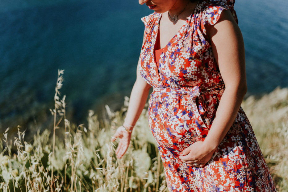 Photographe maternité - Photographe grossesse - Perpignan - Femme enceinte qui touche des fleurs sèches en bord de mer au Cap Béar